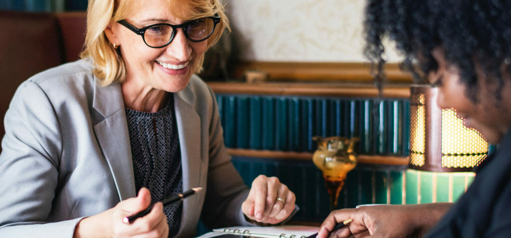 Dos mujeres sentadas una frente a la otra en una mesa hacen un intercambio de conocimientos.