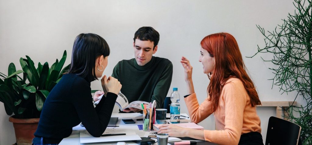 Drie mensen die op kantoor rond een tafel zitten en terwijl ze praten, hun soft skills toepassen.