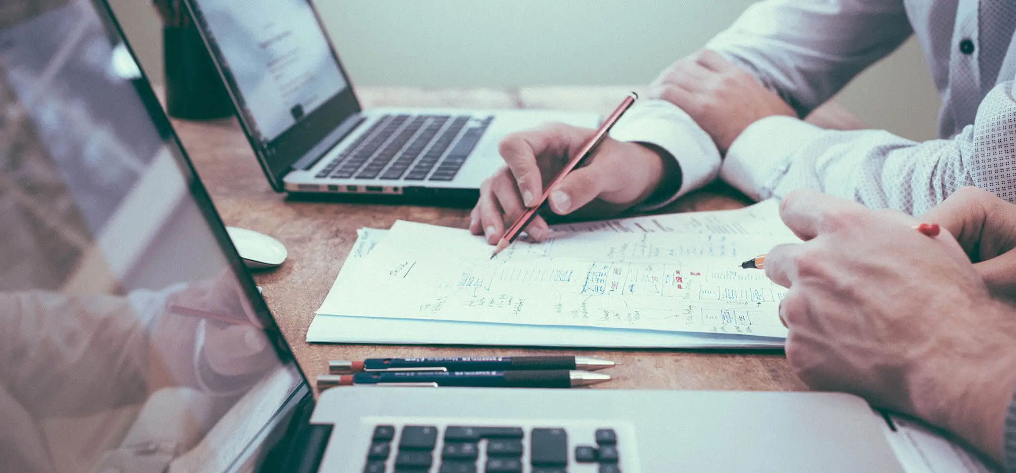 Dos personas creando un programa de formación en una mesa con folios, lápices y ordenadores portátiles.