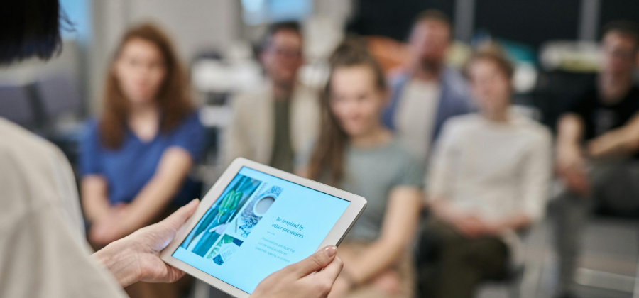 A person using a tablet to present information on how to make online courses more interactive to a seated audience in a room.